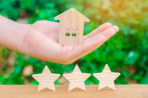 Hand holding a wooden model of house with 3 stars underneath