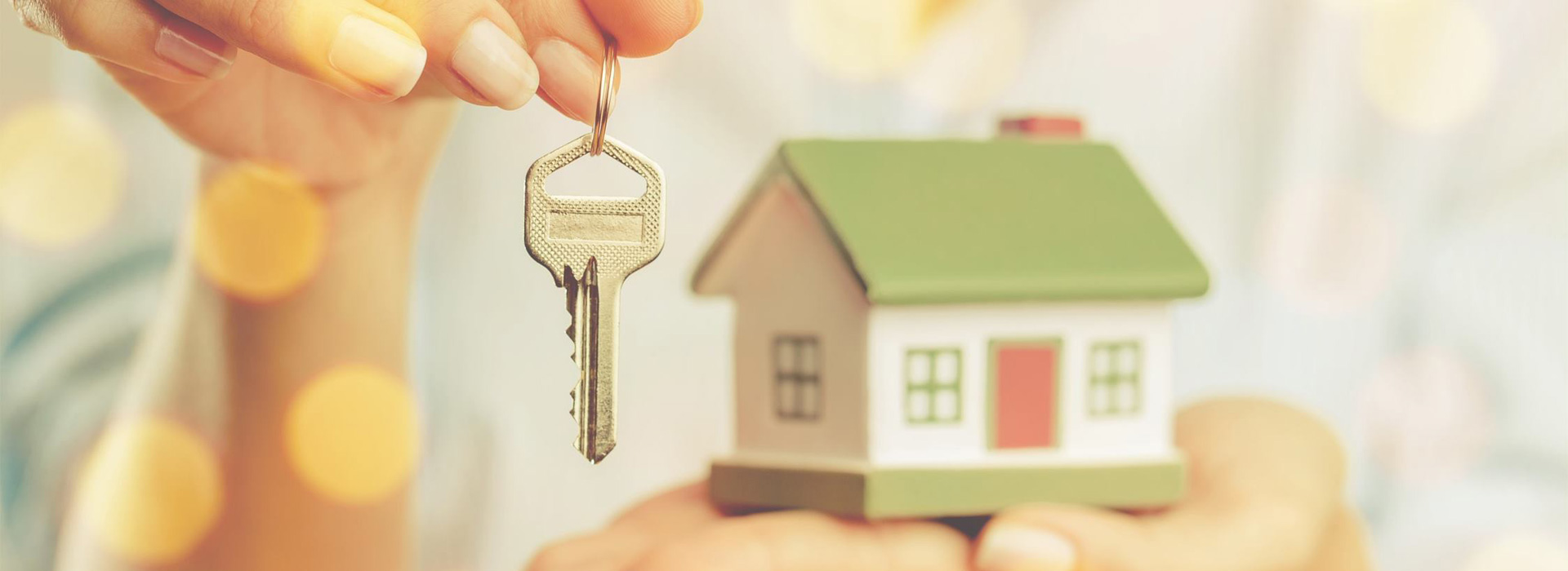 Woman holding keys in one hand and a model wooden house in the other